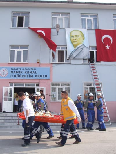 <p><font size="2"><font face="Arial"><strong>Olası Afetler İ&ccedil;in Uygulamalı Bilgiler Verildi<br /><br /></strong>Olası afetler karşısında alınacak tedbirler hakkında &ccedil;eşitli konuşmaların yapıldığı programda Namık Kemal İlk&ouml;ğretim Okulu &ouml;ğrencilerinin ilk yardım ve afetlerle ilgili hazırladığı oyunlar b&uuml;y&uuml;k beğeni topladı. <font color="#333399">Okul bah&ccedil;esinde d&uuml;zenlenen etkinlikte; Sakarya B&uuml;y&uuml;kşehir Belediyesi İtfaiyesi ekipleri tarafından ger&ccedil;eğini aratmayan yangın kurtarma tatbikatı yapıldı, 112 Acil Servis g&ouml;revlilerince yaralılara yapılacak ilk yardım hakkında uygulamalı bilgiler verildi, Kızılay tarafından okul bah&ccedil;esine yardım &ccedil;adırı kuruldu.</font> <br /><br /><strong>&Ouml;ğrenciler, Platform &Uuml;zerine Atlayarak Kurtuldu<br /><br /></strong>Afet eğitimi etkinliğinin en heyecanlı b&ouml;l&uuml;m&uuml; ise ger&ccedil;eğini aratmayan sahnelerin yaşandığı yangın tatbikatı oldu.<font color="#333399"> Senaryo gereği okulda &ccedil;ıkan yangında ilk olarak alt kattaki &ouml;ğrencilerin hızlı bir şekilde binayı boşaltması sağlanırken, &uuml;st katlarda mahsur kalan &ouml;ğrenciler itfaiye ekipleri tarafından merdivenli ara&ccedil;larla pencerelerden indirildi.</font> Bazı &ouml;ğrenciler ise havayla şişirilen platform &uuml;zerine atlayarak kurtarıldı. </font></font></p><p><font size="2"><font face="Arial"><strong>&Ouml;ğrenciler Heyecan İ&ccedil;inde İzledi<br /><br /></strong><font color="#333399">Tatbikatta yaralanan &ouml;ğrencilere ilk m&uuml;dahaleyi yapan 112 Acil Servis doktorları ve g&ouml;revlileri yaralı &ouml;ğrencileri kısa s&uuml;rede ambulanslarla hastanelere g&ouml;t&uuml;rd&uuml;</font>. Protokol &uuml;yeleri, &ouml;ğrenciler ve veliler heyecanlı sahnelerin olduğu programı b&uuml;y&uuml;k bir dikkat ve heyecan i&ccedil;inde izledi.</font></font>&nbsp;</p>